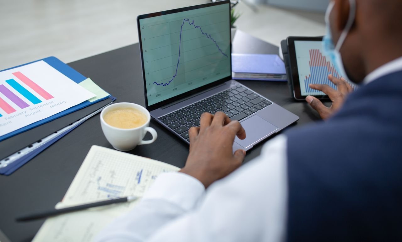 Focused professional analyzing data with laptop and tablet in modern office setting.
